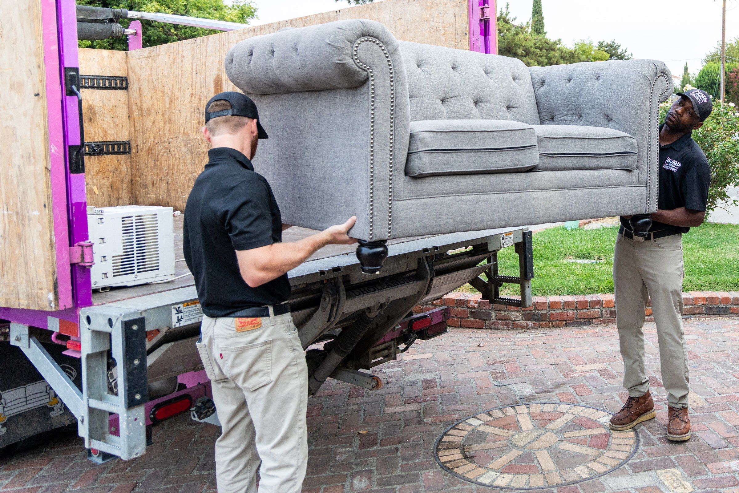 Two Dump Ninja crew members loading a gray couch into the 21-yard truck at a Woodland home