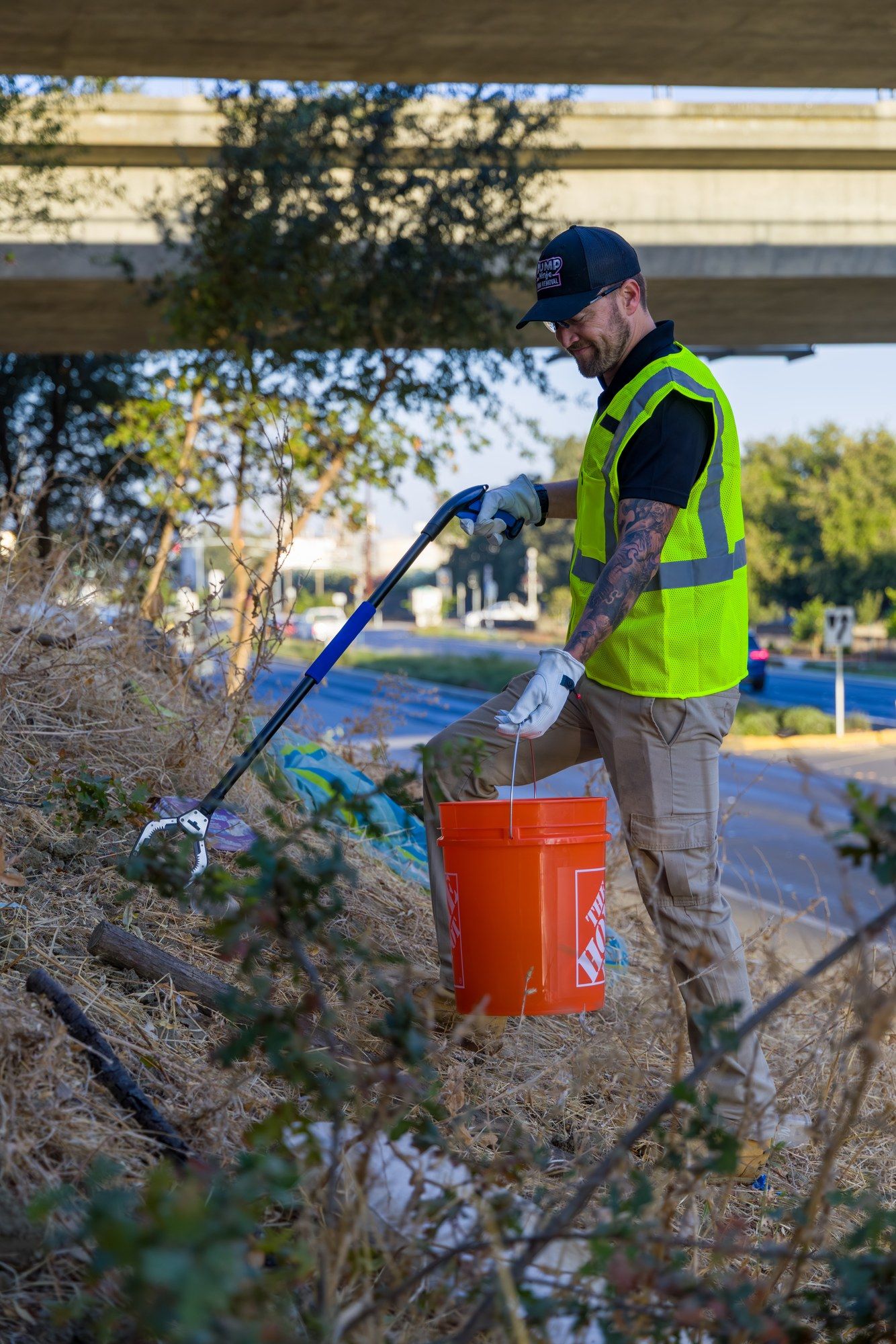 A Dump Ninja crew member clearing litter and debris from a roadside embankment with a grabber and bucket