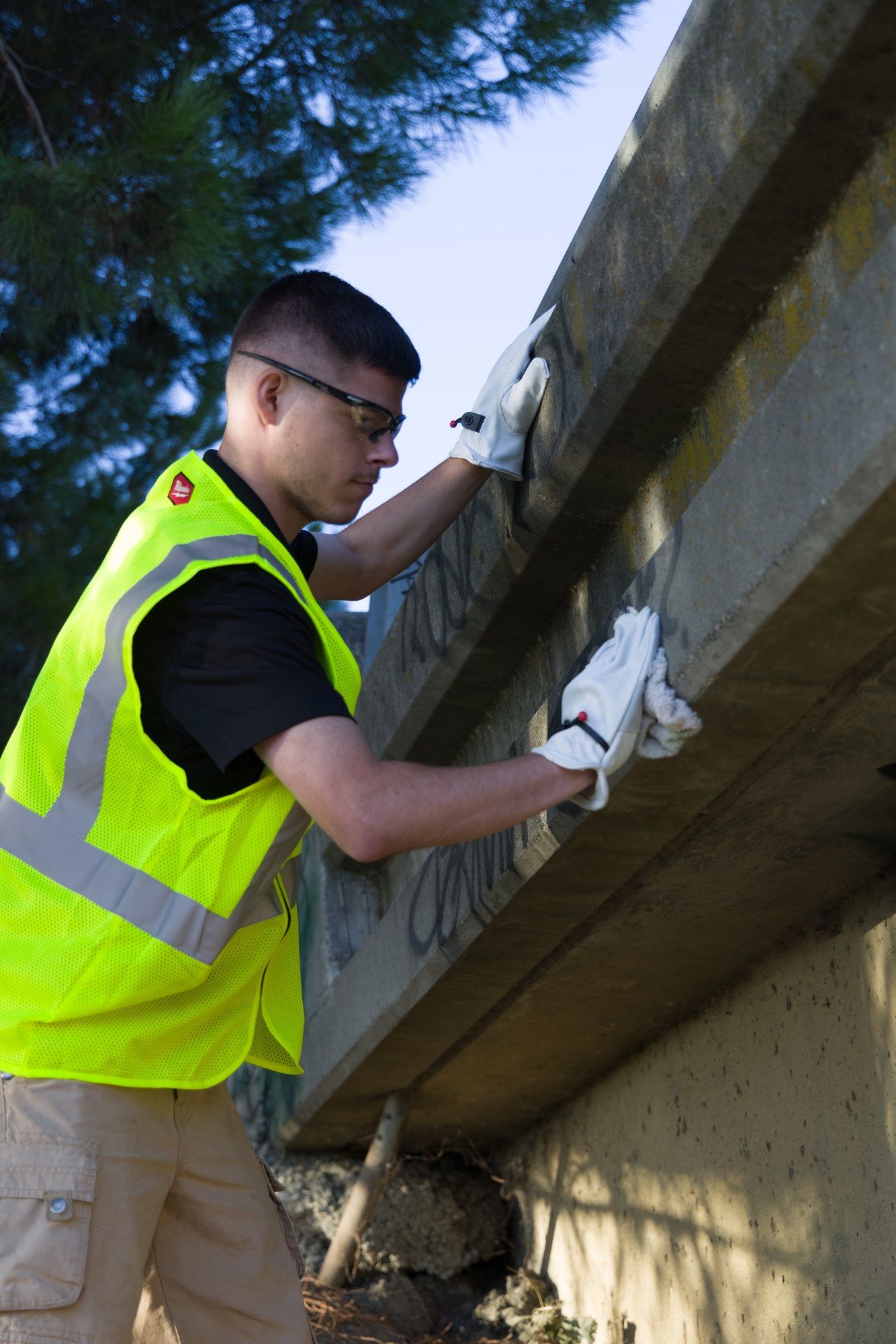 Dump Ninja crew member wiping graffiti from a surface beneath a guardrail in Yolo County