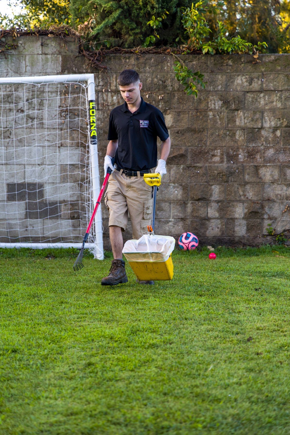 Dump Ninja crew member with tools staged beside a soccer goal on a shared lawn in Woodland, ready to service pet waste stations