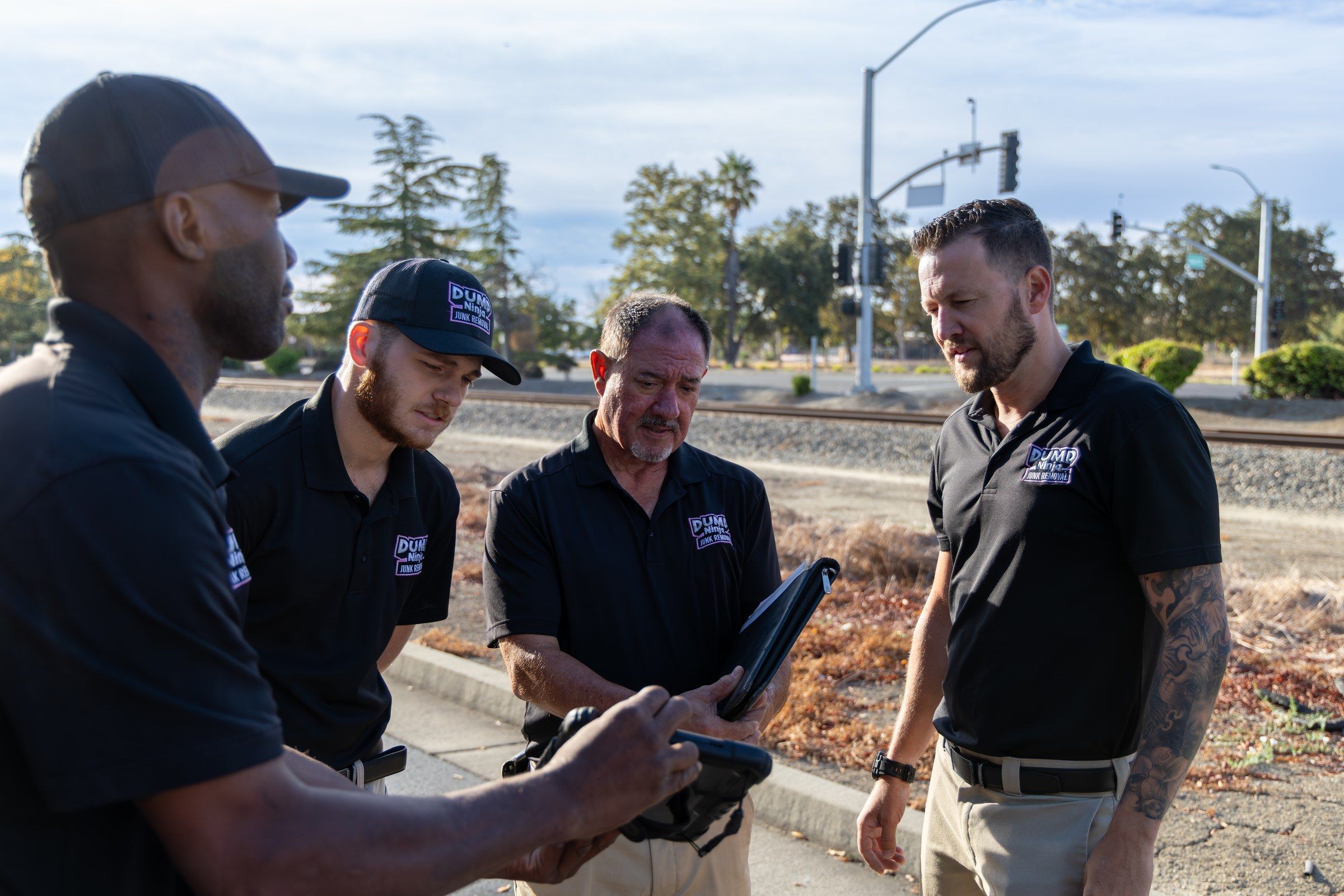Dump Ninja crew reviewing a site on a tablet beside railroad tracks